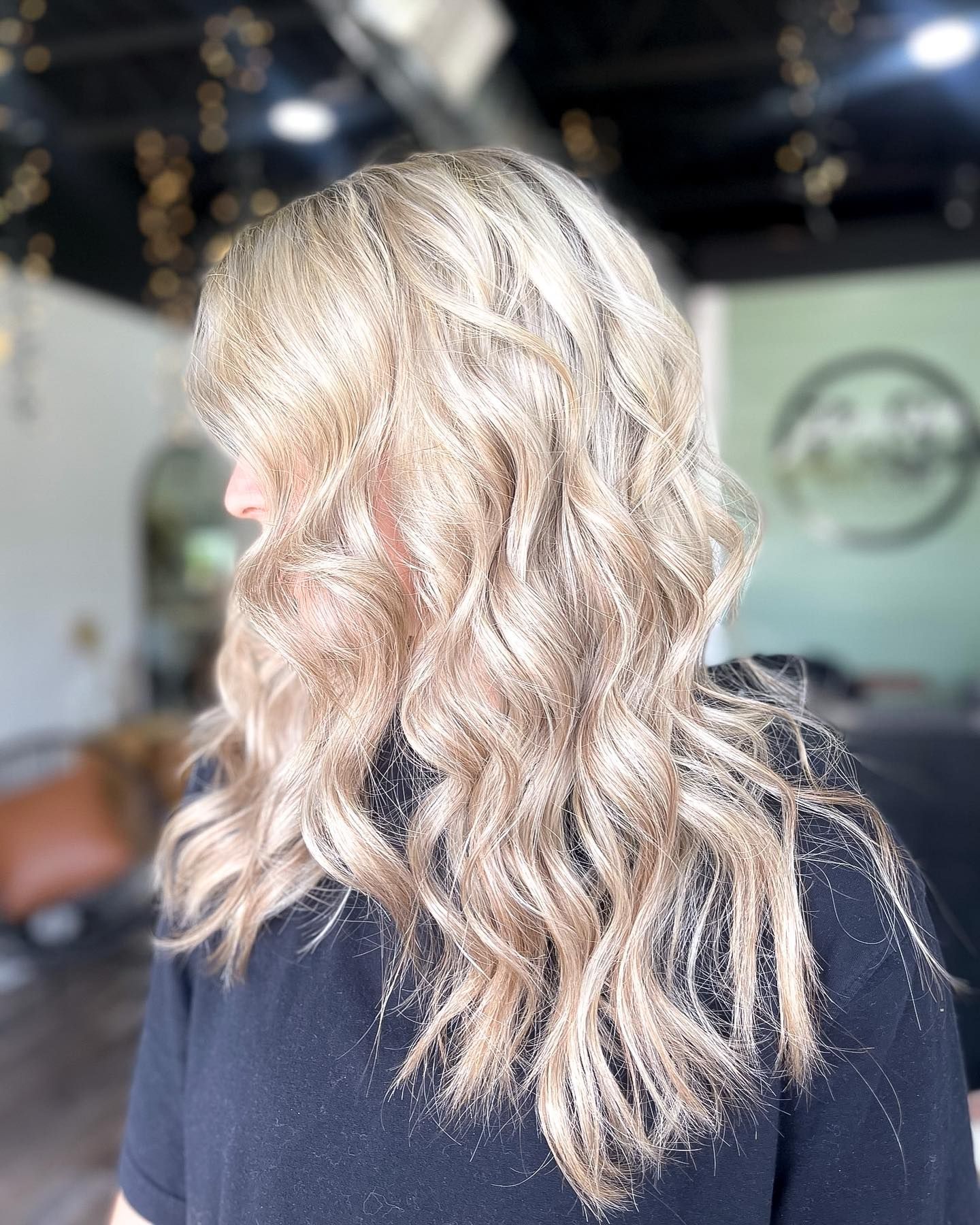 Woman with wavy blonde hair, slightly turned, in a salon.