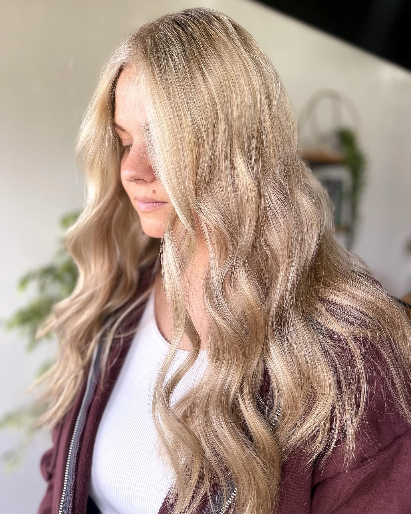 Woman with long, wavy blonde hair wearing a white shirt and burgundy jacket.