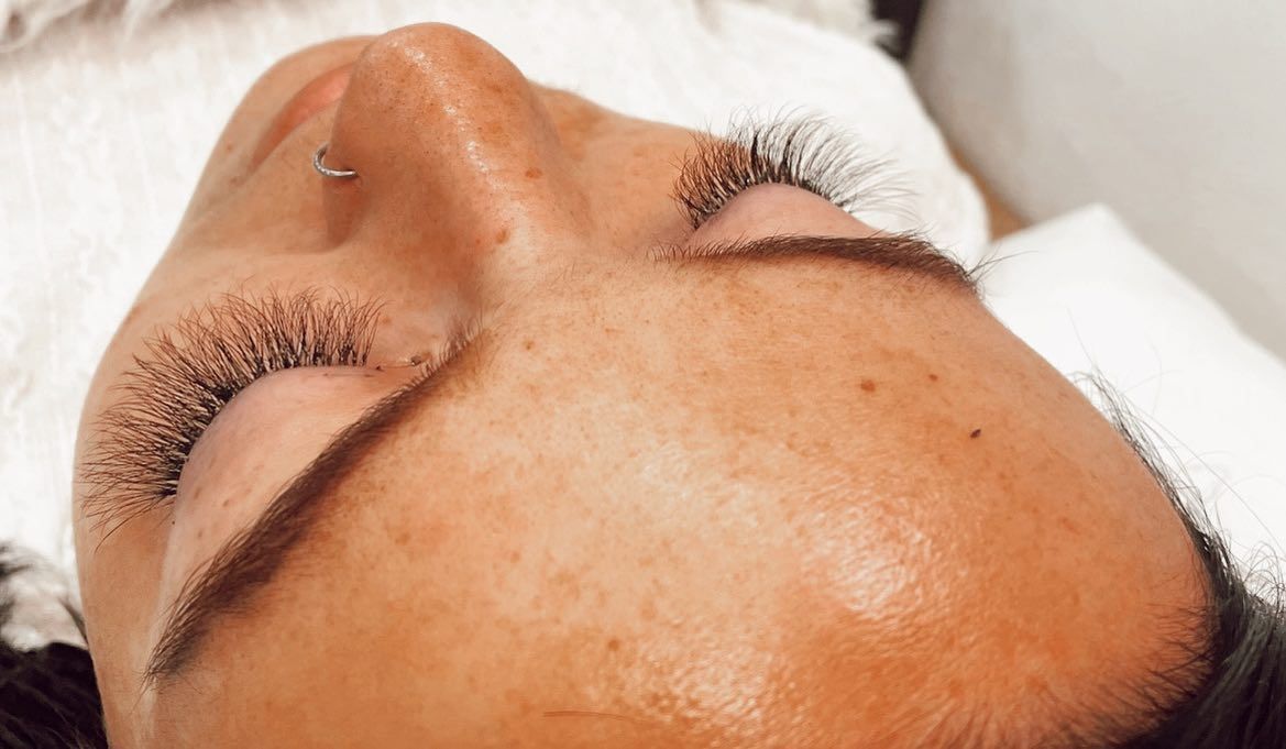 Close-up of a person's face with closed eyes. They have long, full eyelashes and a nose piercing.