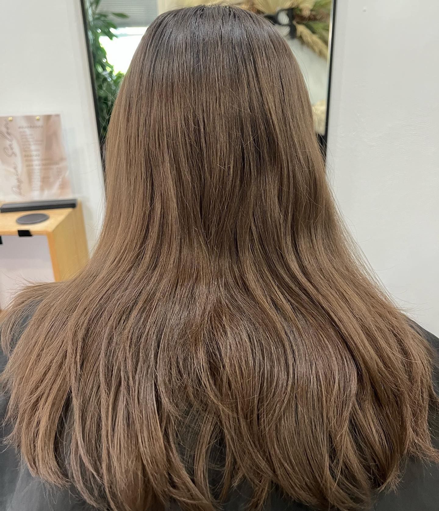 Brown hair, textured, falls to mid-back. Viewed from behind in a salon setting.
