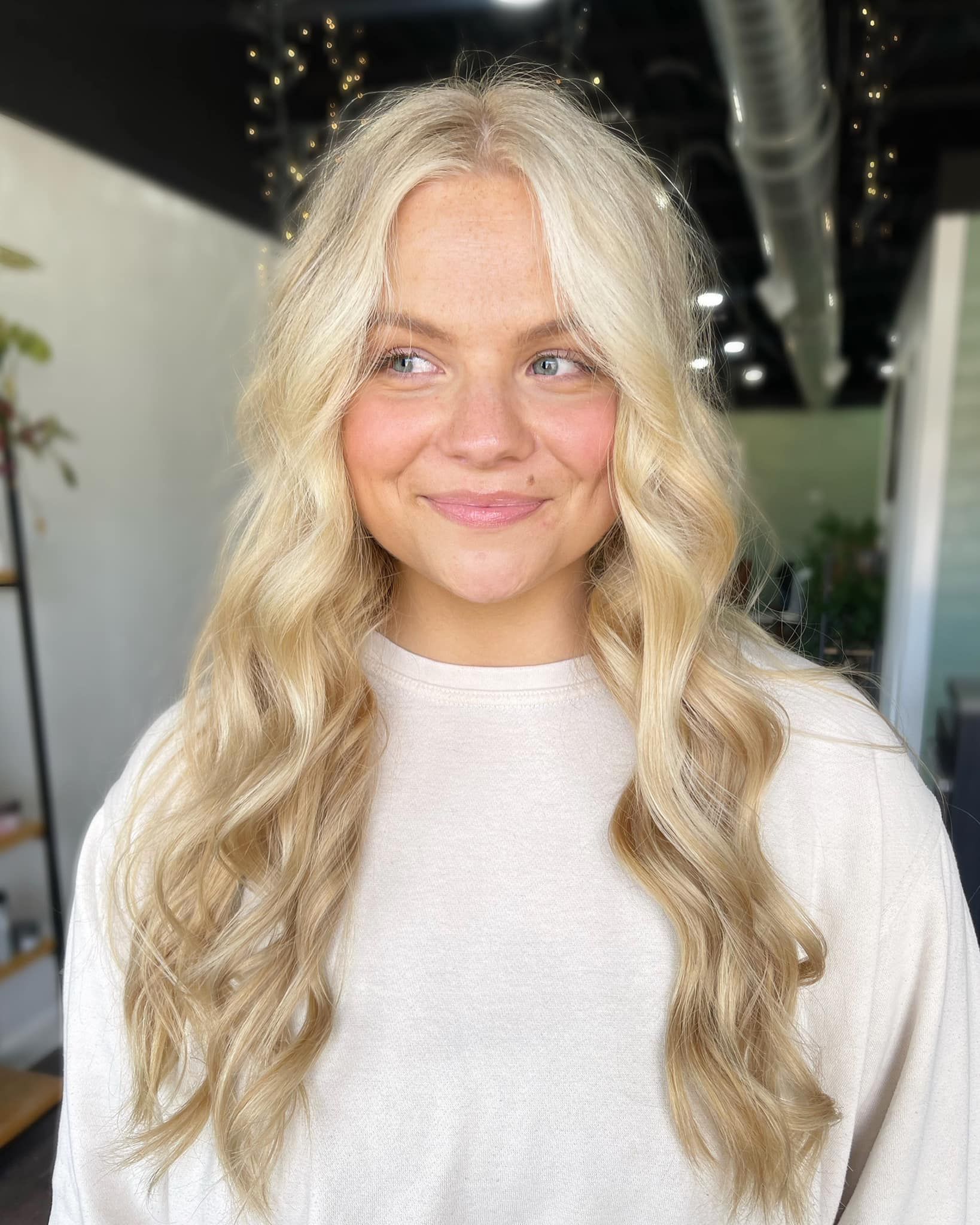 Woman with wavy blonde hair, smiling in a well-lit setting.