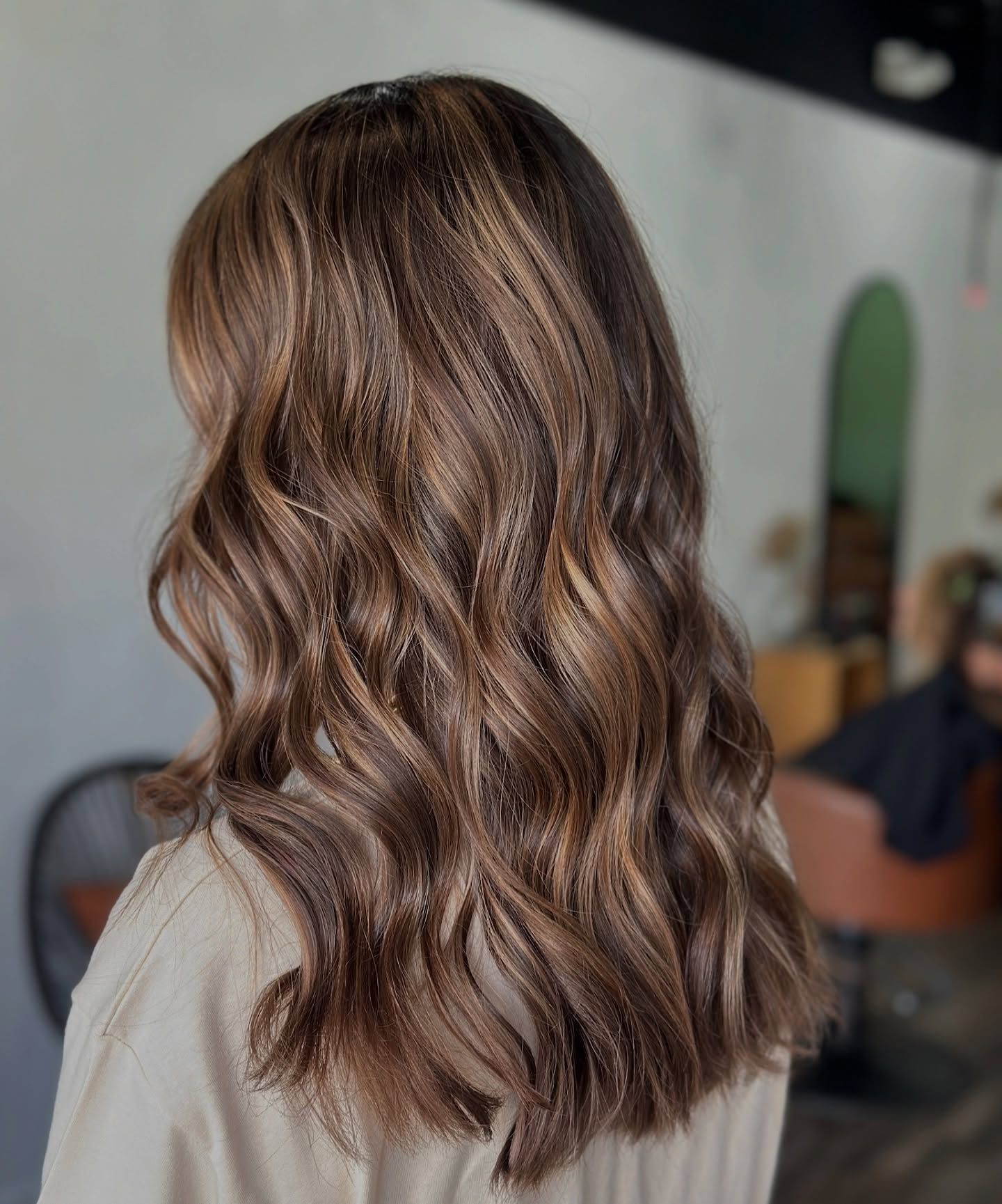 Woman with wavy brown hair with highlights, styled in a salon.