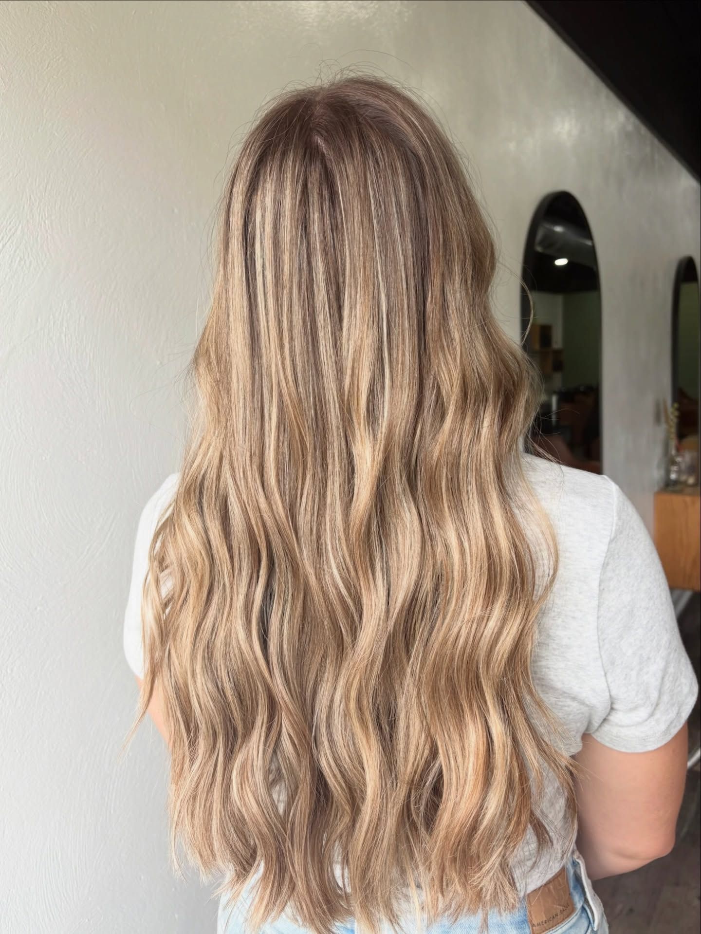Woman with long, wavy blonde hair with highlights, standing indoors.