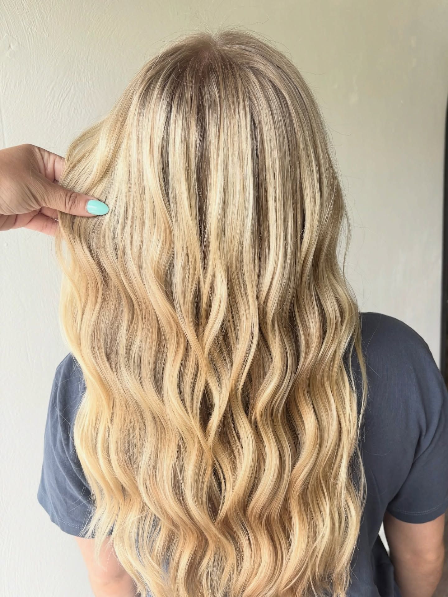 Blonde wavy hair with darker roots, hand holding a strand.