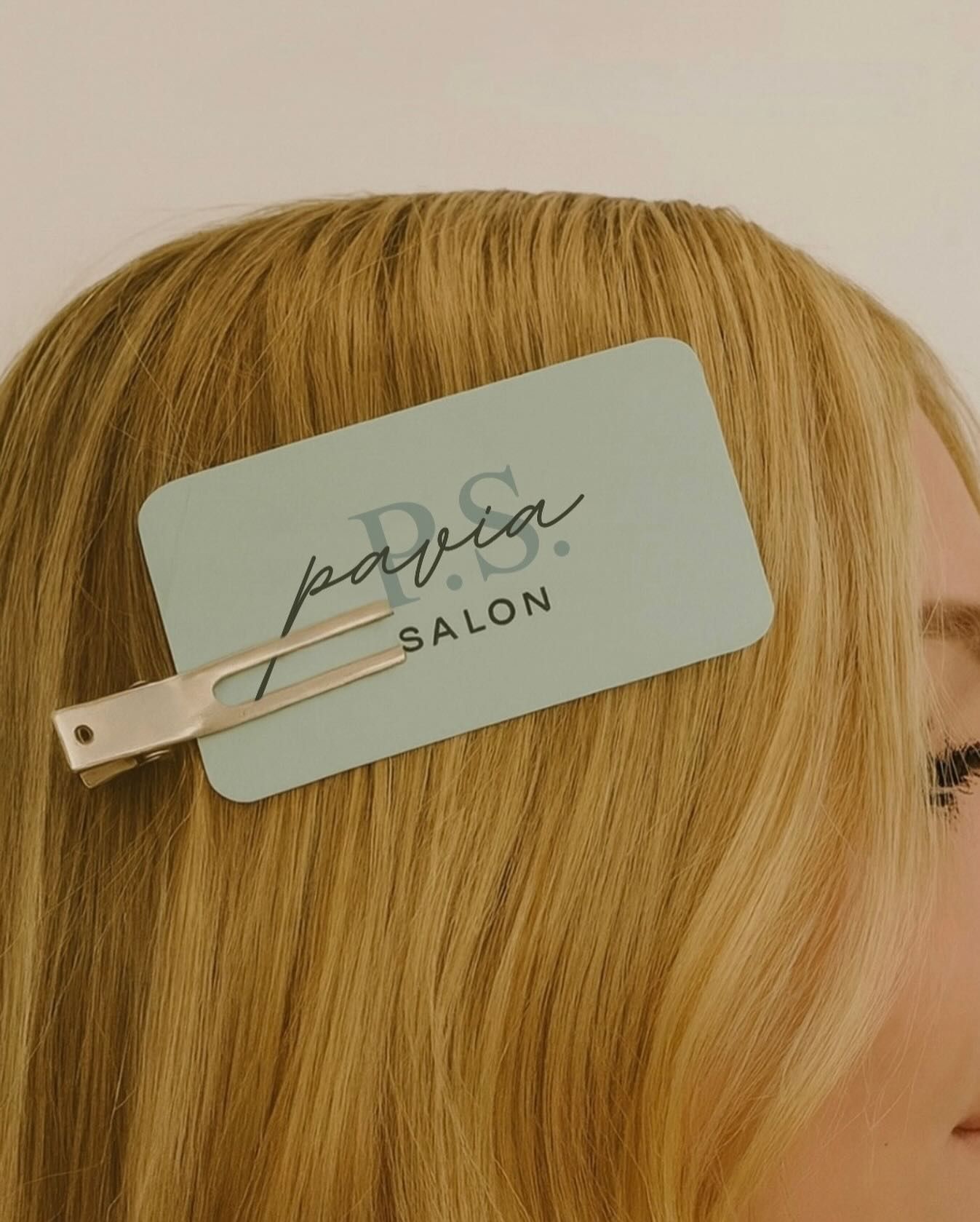 Blond hair with a hair clip holding a blue P.S. Salon gift card.