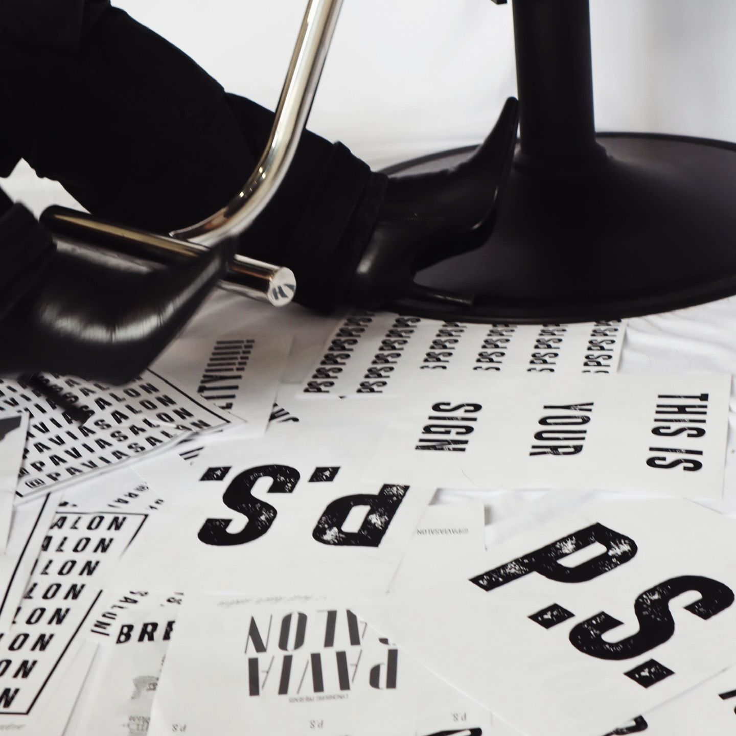 Black high heel shoe and chair leg with scattered white papers, text: 