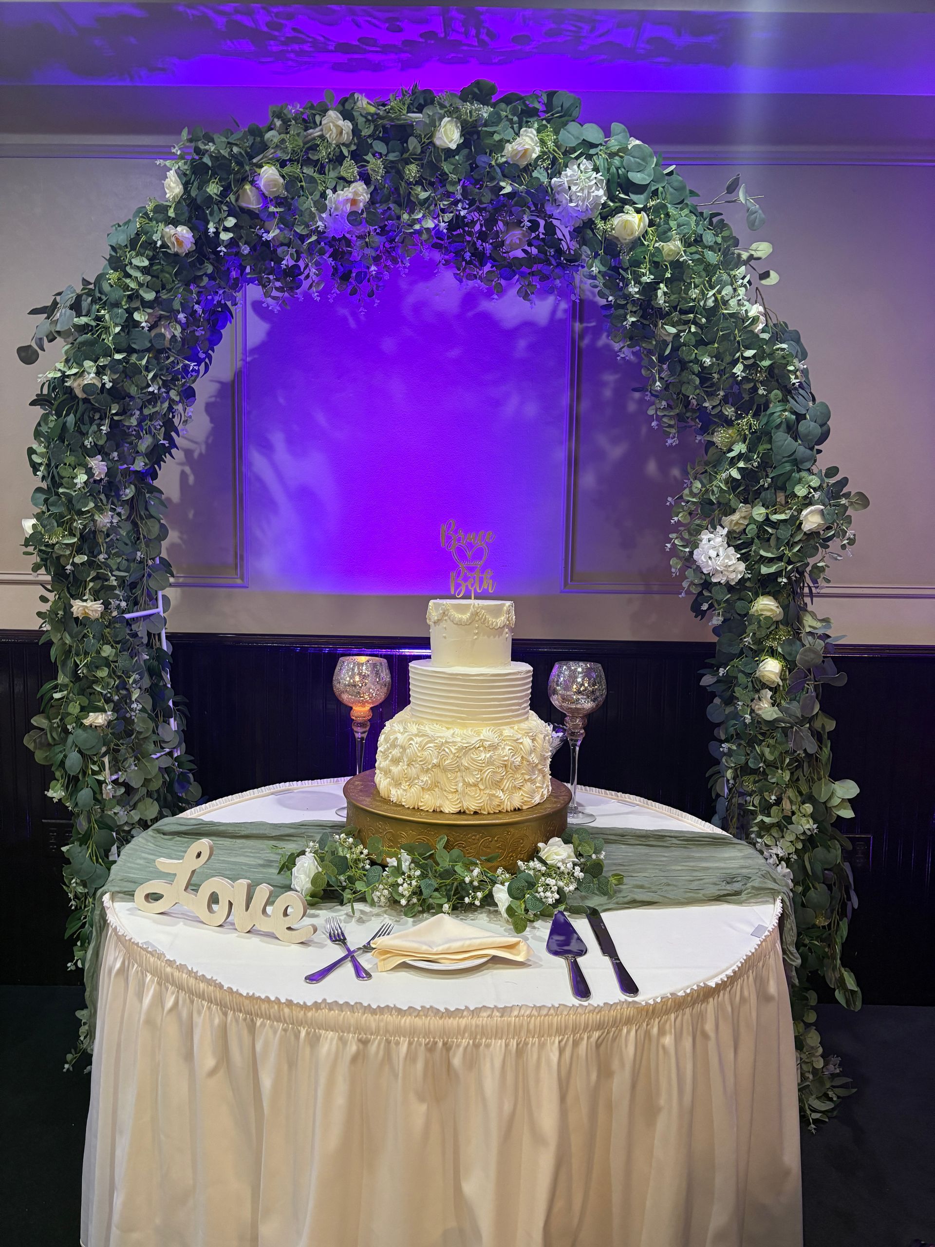 Round banquet table set for a formal event with white tablecloth, silverware, and folded napkins. Blue-lit room.