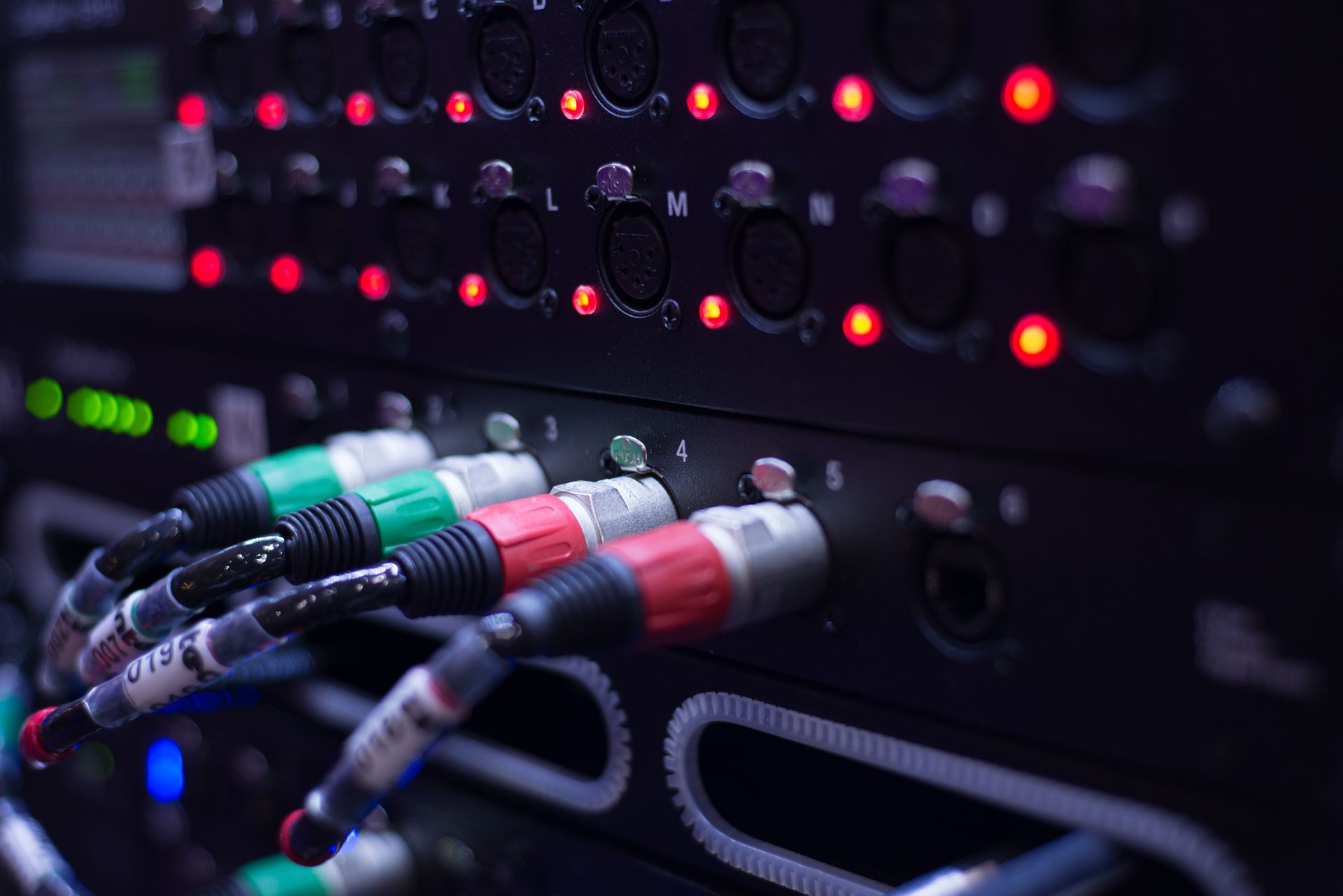 Close-up of a black audio equipment rack with colorful cables plugged in and red lights illuminated.