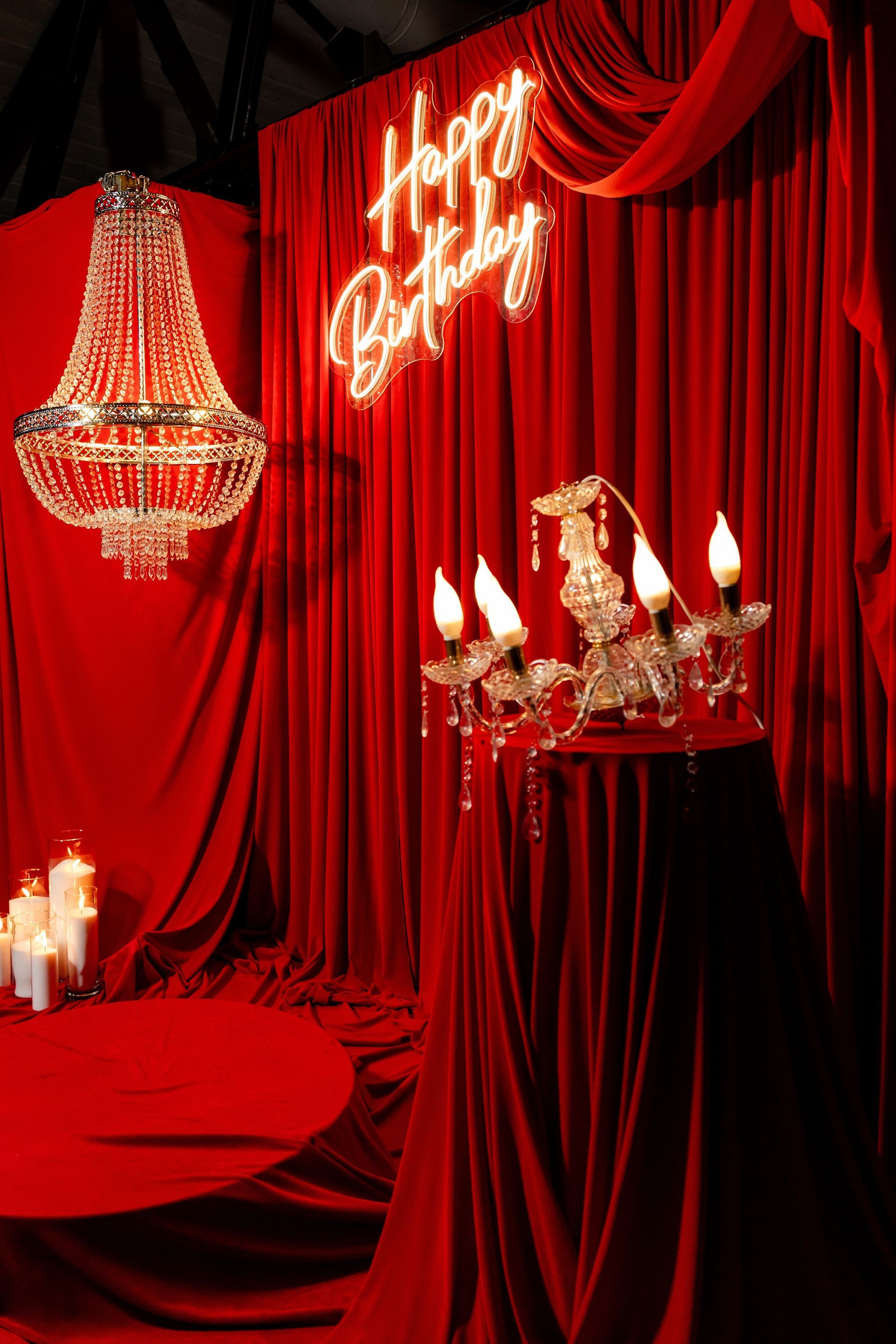 Red birthday backdrop with a chandelier, candles, and a neon 