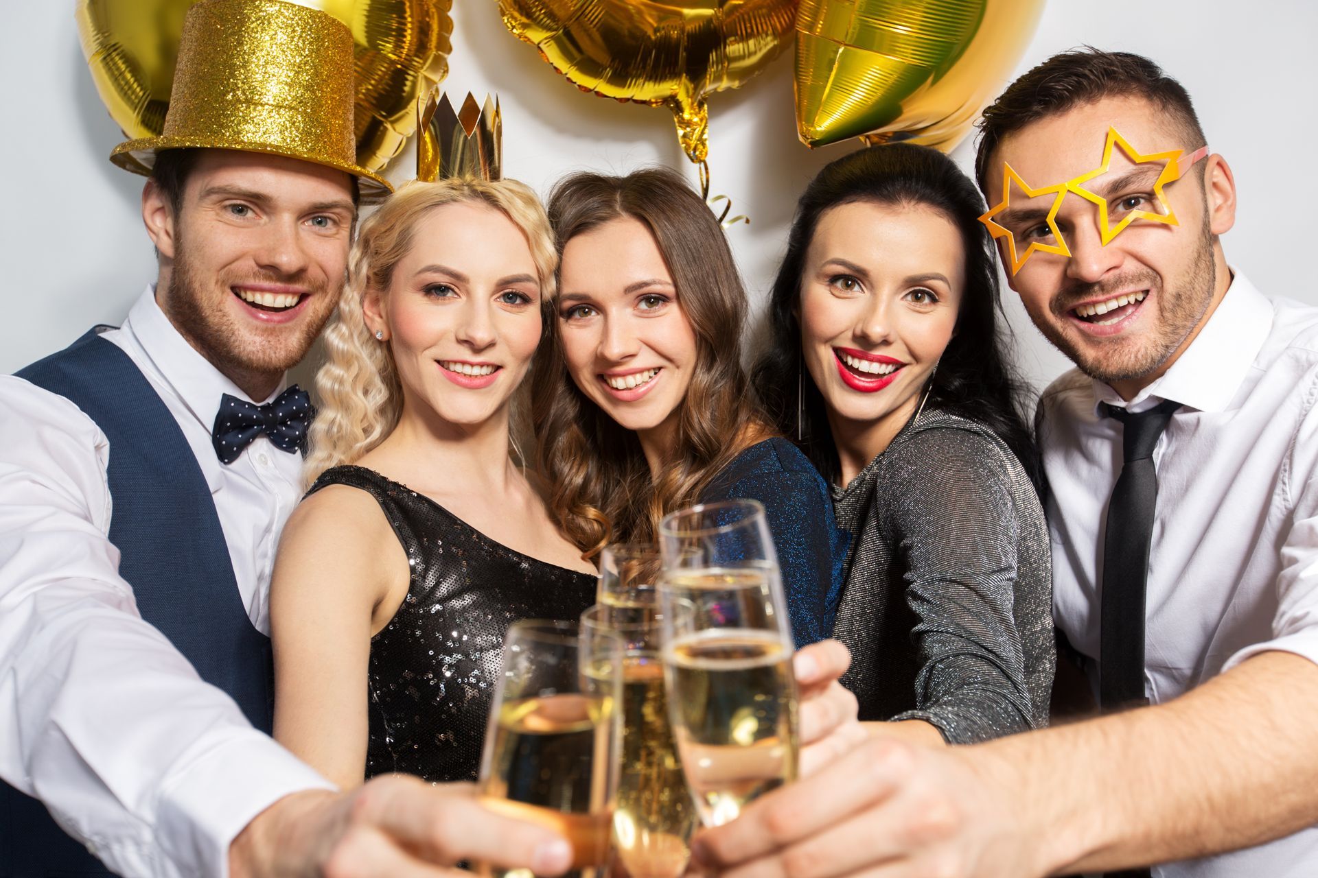 Five people toasting champagne at a party, gold balloons in background.