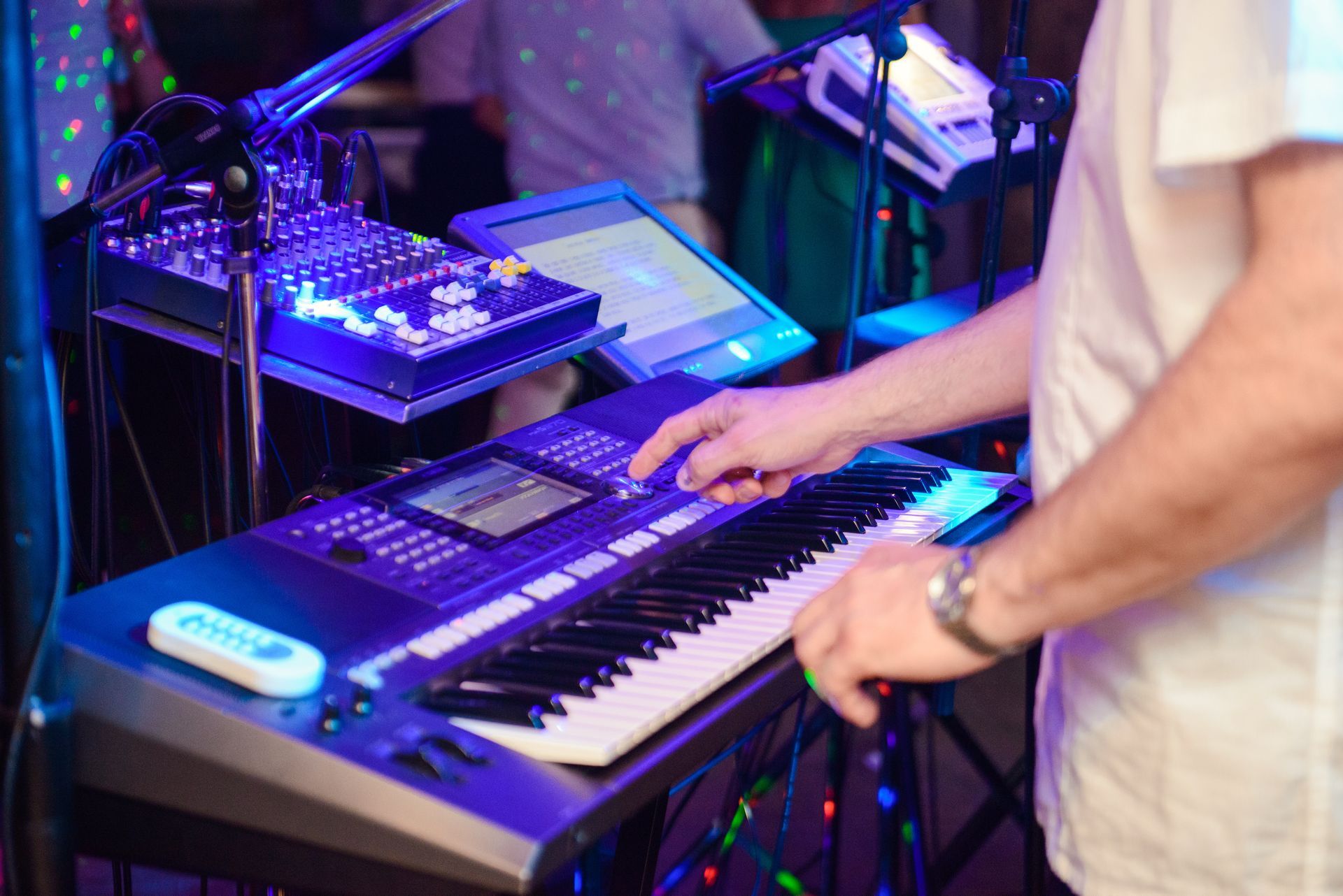 Keyboardist with a keyboard, mixing board, and tablet, lit by blue stage lights.