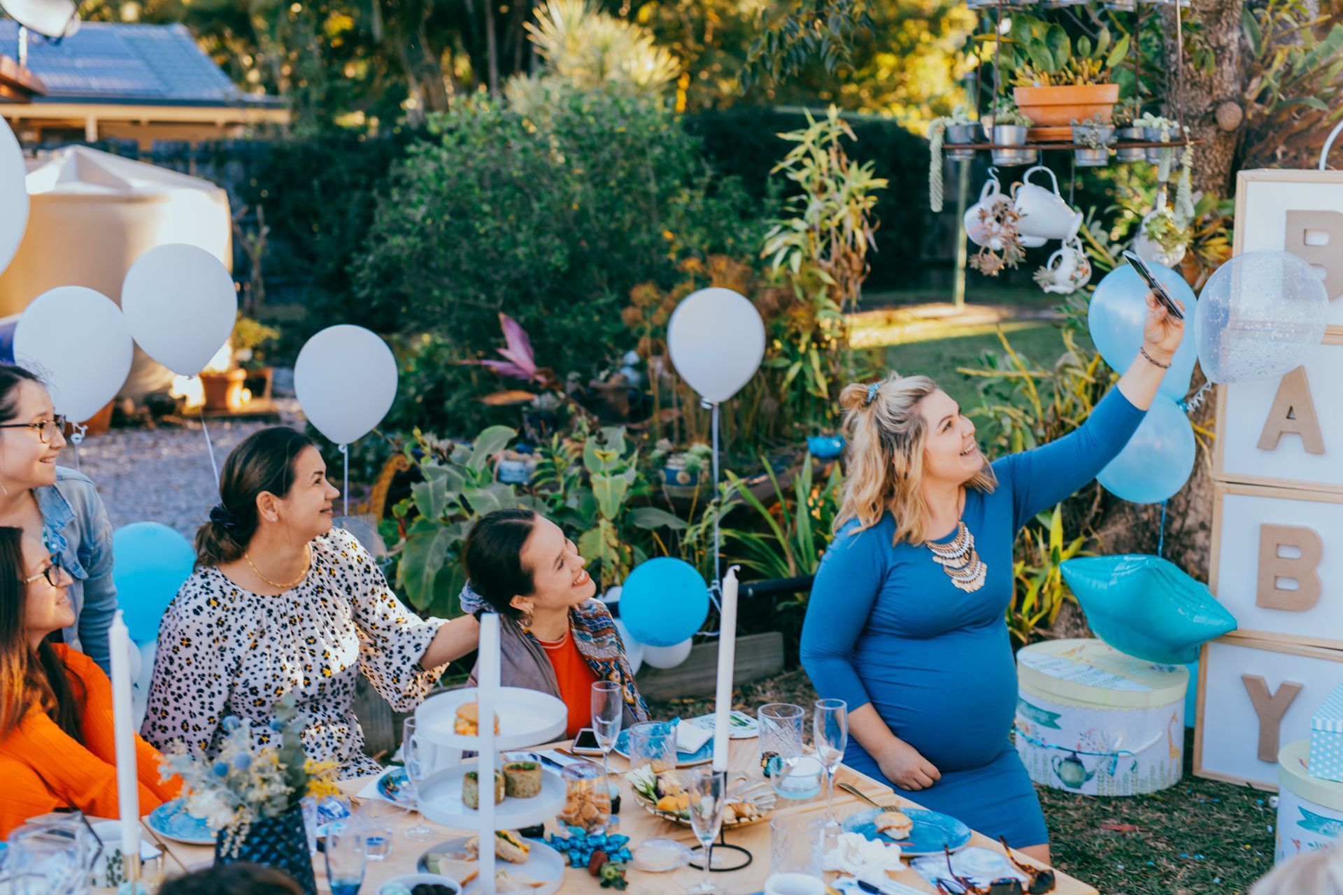 Outdoor baby shower with pregnant woman in blue dress, balloons, and 