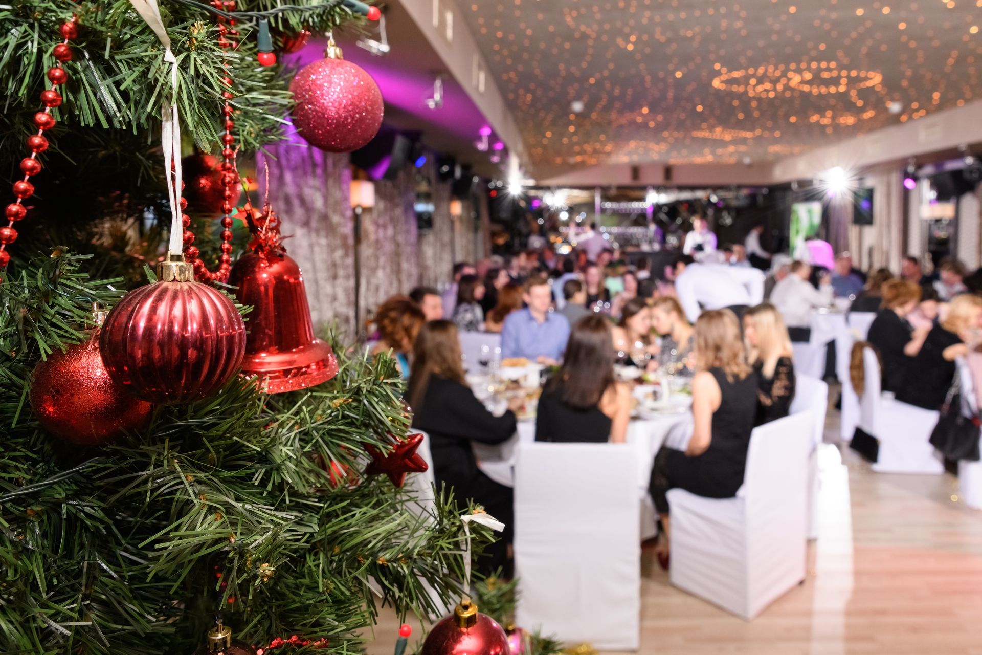 Christmas tree decorated, blurred view of people at tables in a festive dining room.