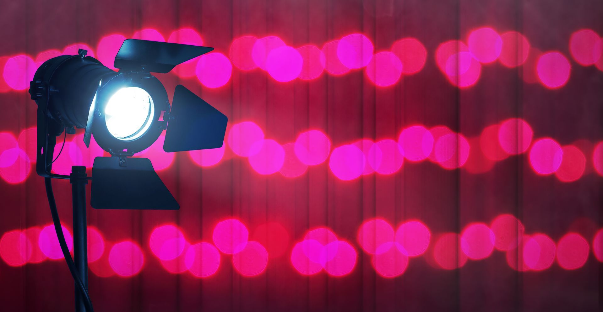 Spotlight illuminates a stage, casting a bright beam against a blurred backdrop of pink lights.