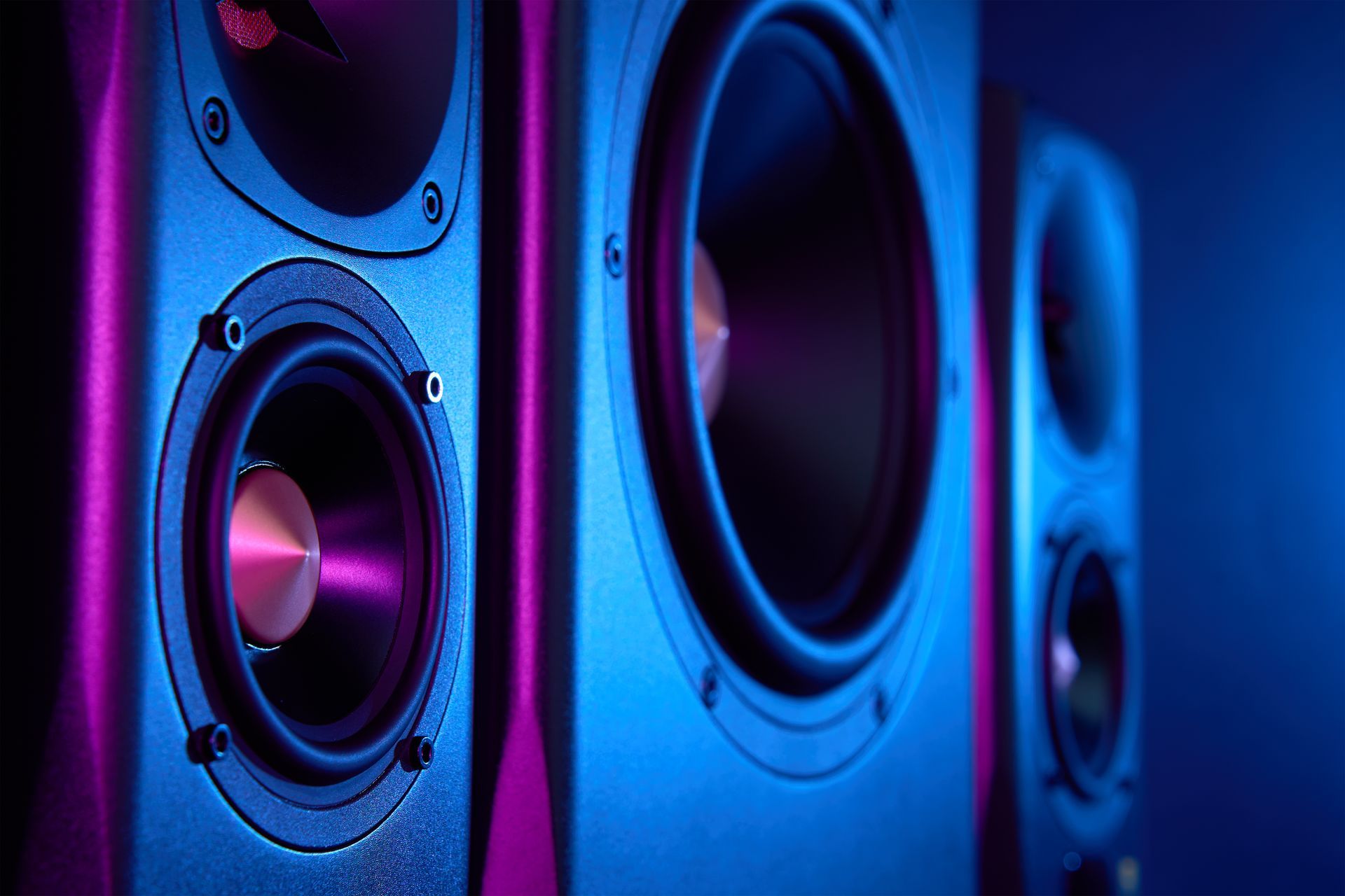 Three black speakers with glowing purple and blue lighting.