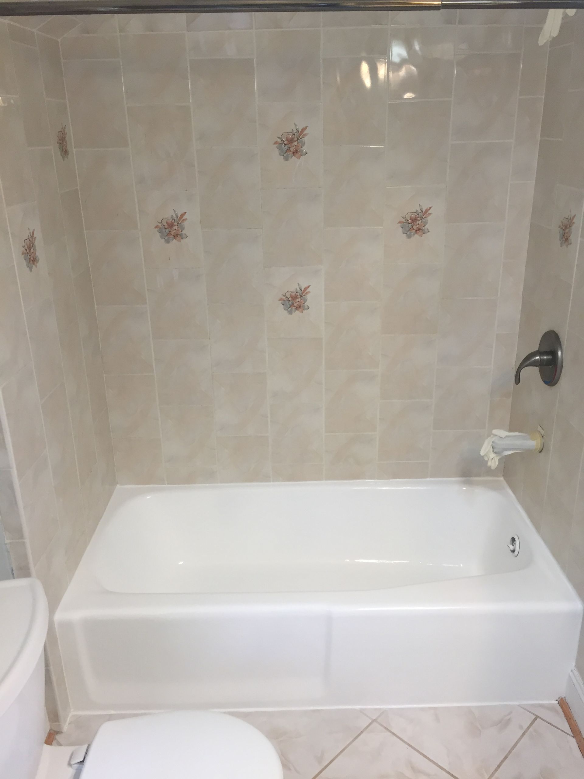 A white bathtub with tan tile surround, a dark faucet, and decorative brown floral tiles in a bathroom setting.