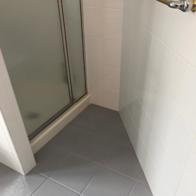 Bathroom corner with gray tiled floor and white tiled walls. Shower door with frosted glass is on the left.