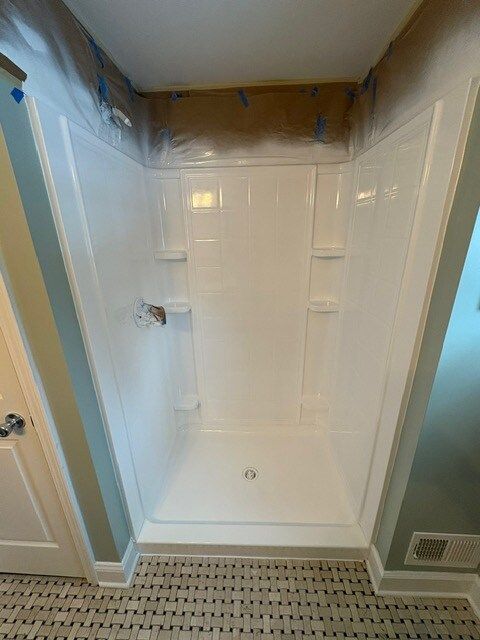 A white shower stall, newly installed, is set against tiled flooring and painted walls.