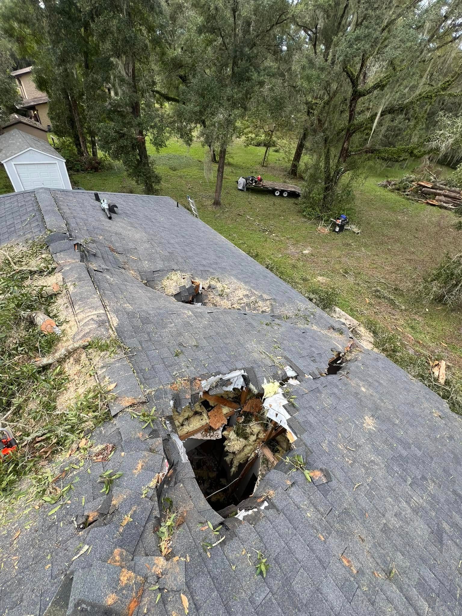 Damaged roof with large holes. Green grass and trees in the background.