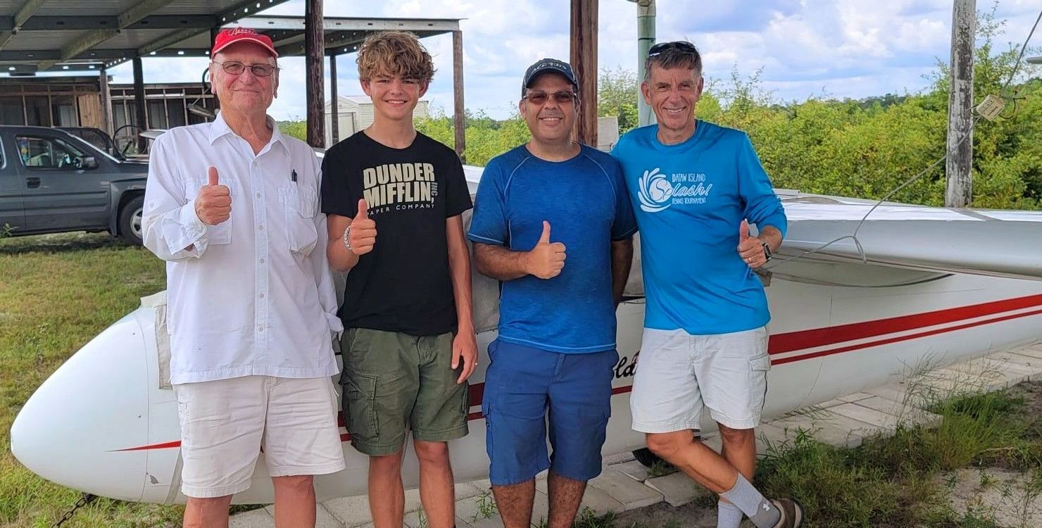 A group of glider pilots, CFIG, FAA instructor, youth glider pilot are standing next to a plane and giving a thumbs up.