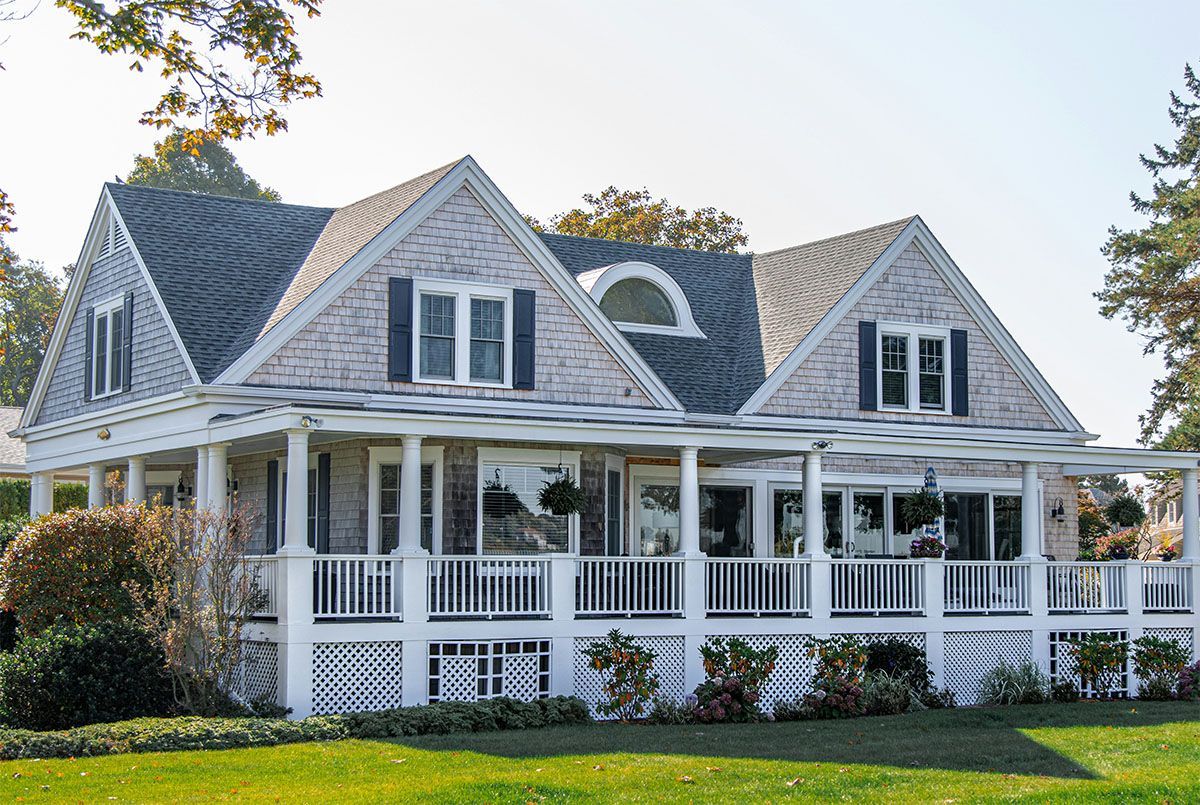 A large white house with a large porch on a sunny day. New asphalt shingles on a white house roof.