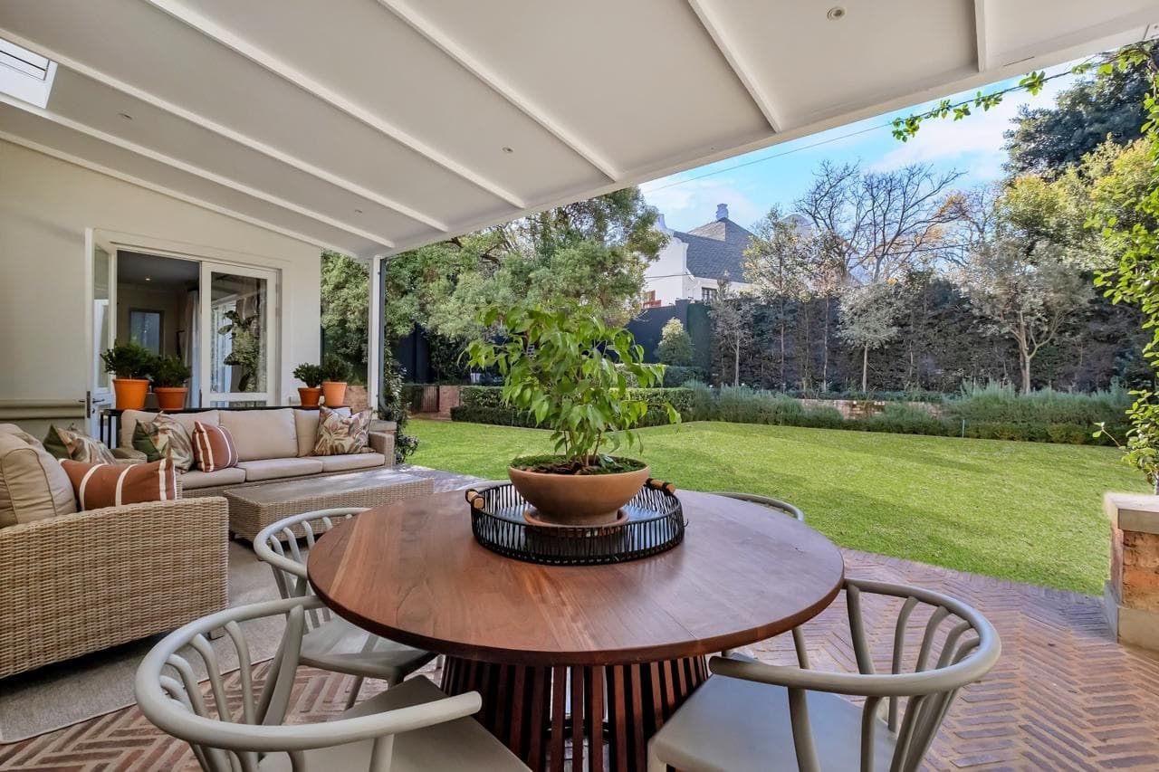 A patio with a couch , chairs and a table with a view of a lush green field.
