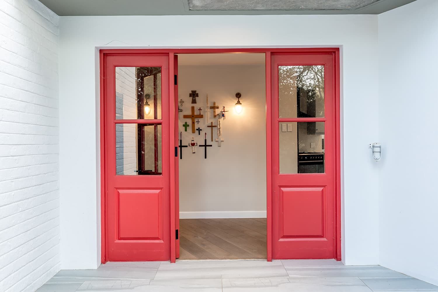 A red door is open to a room with a white brick wall.