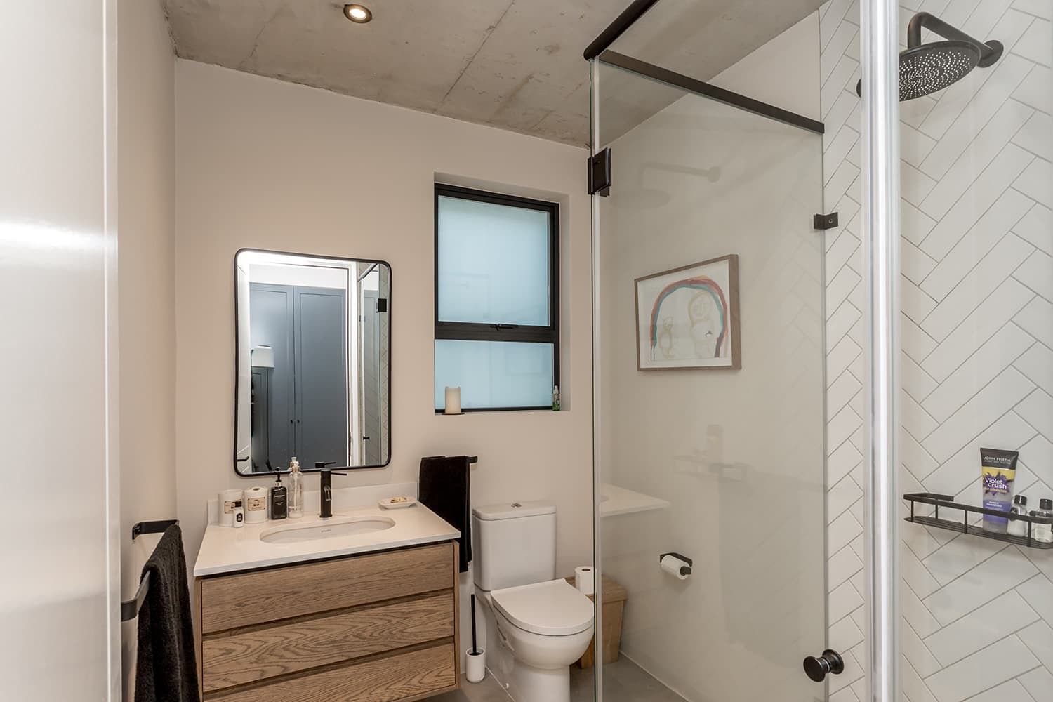 A bathroom with a toilet , sink , mirror and shower.