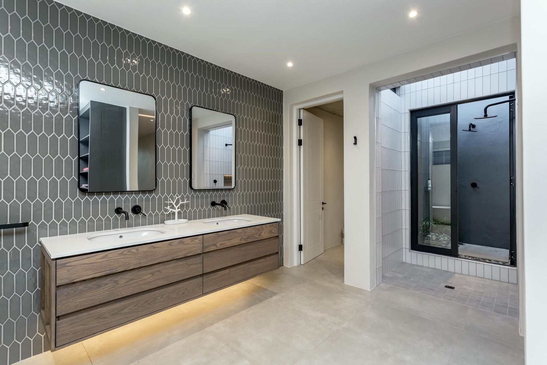 A bathroom with two sinks , two mirrors and a walk in shower.
