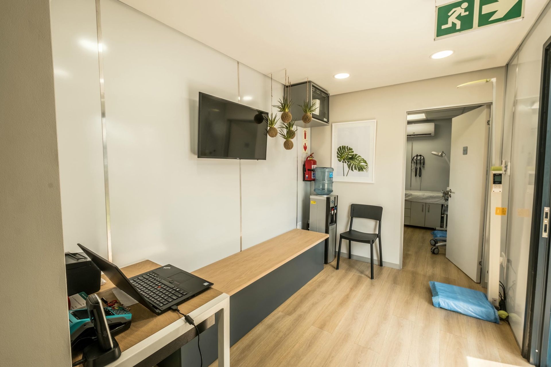 A room with a desk , chairs , a tv and a green exit sign.