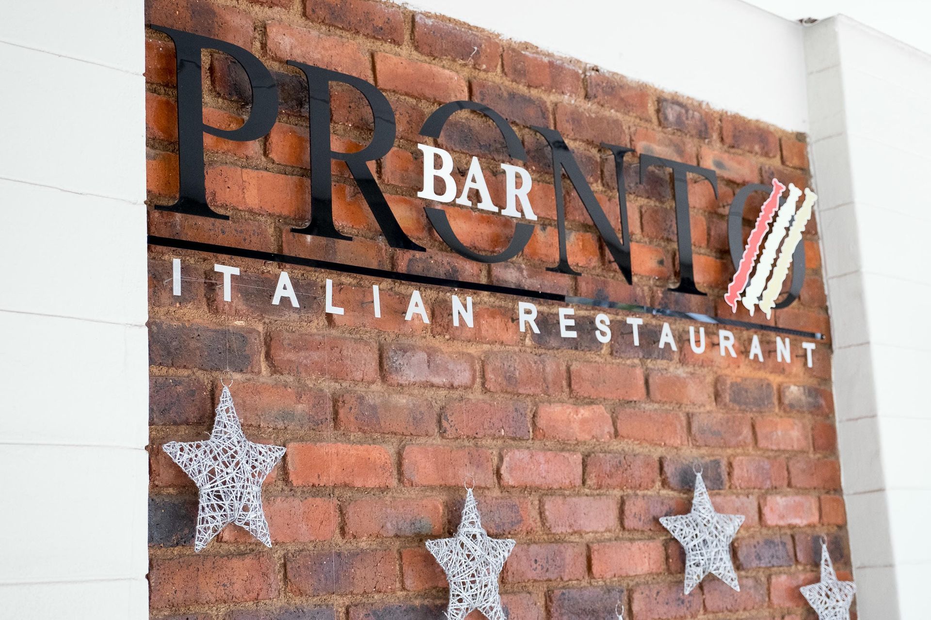 A sign for pronti italian restaurant is on a brick wall.