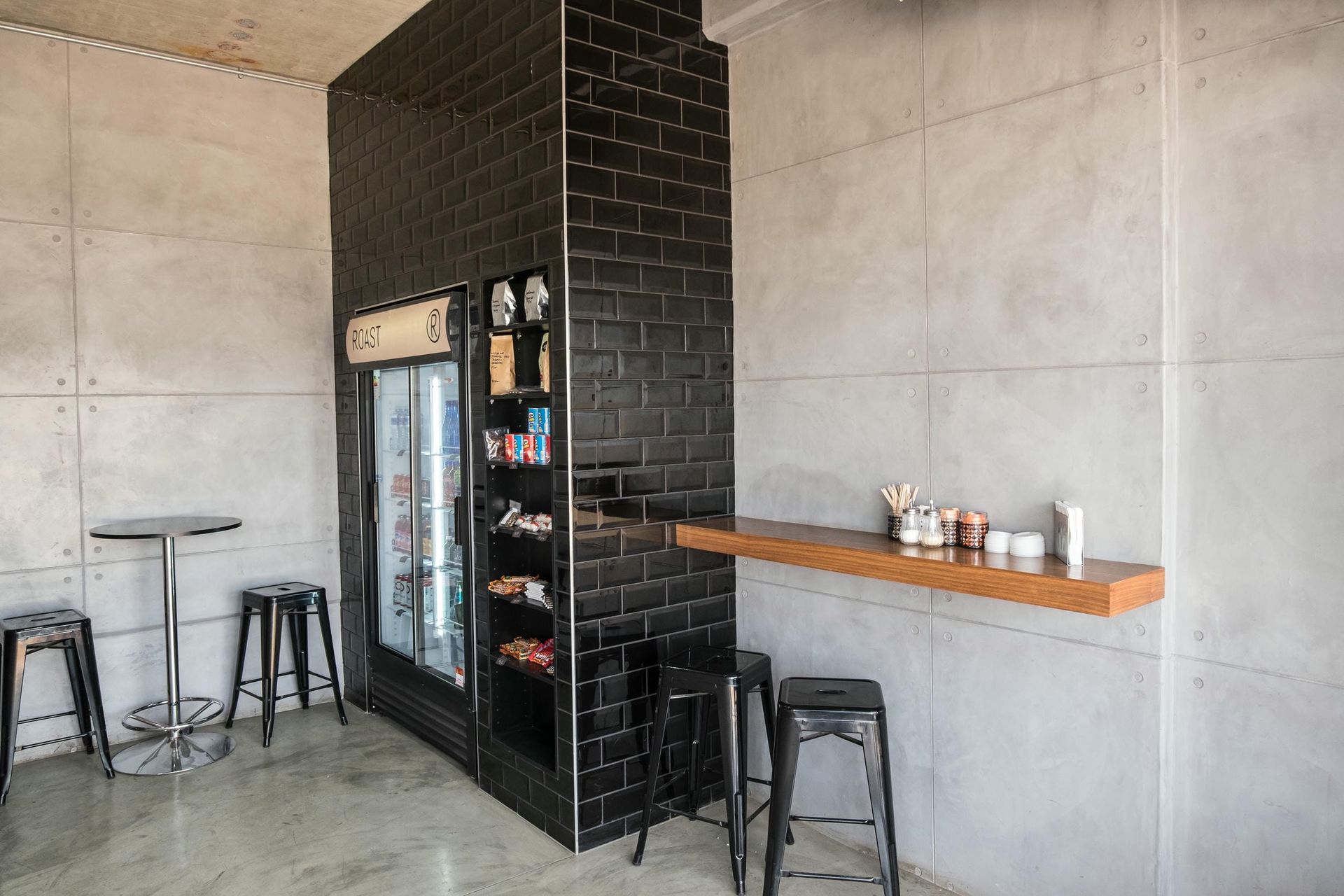 A room with tables and stools and a refrigerator.