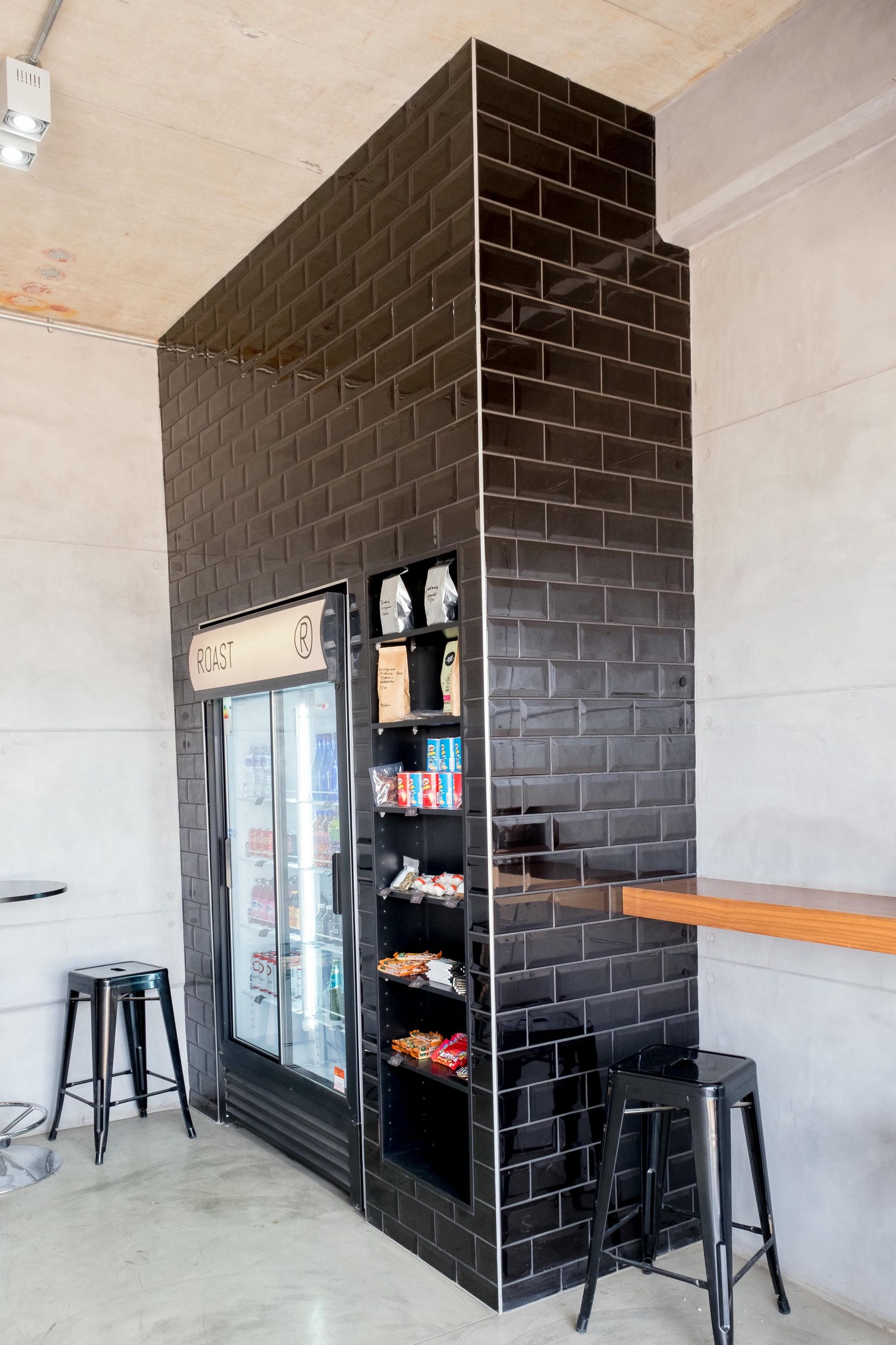 A room with a refrigerator , stools , a table and a brick wall.