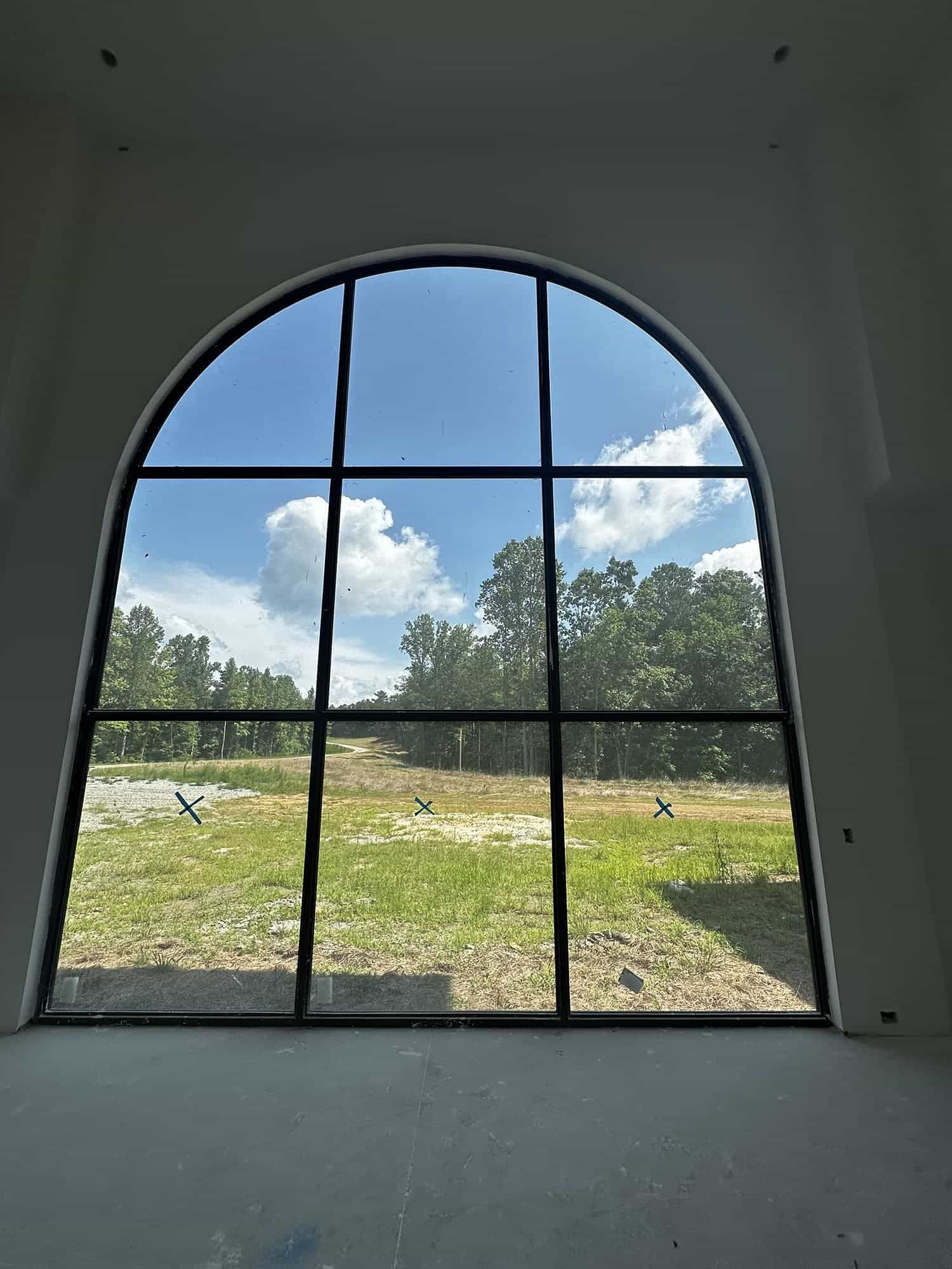 A large arched window with a view of a field and trees.