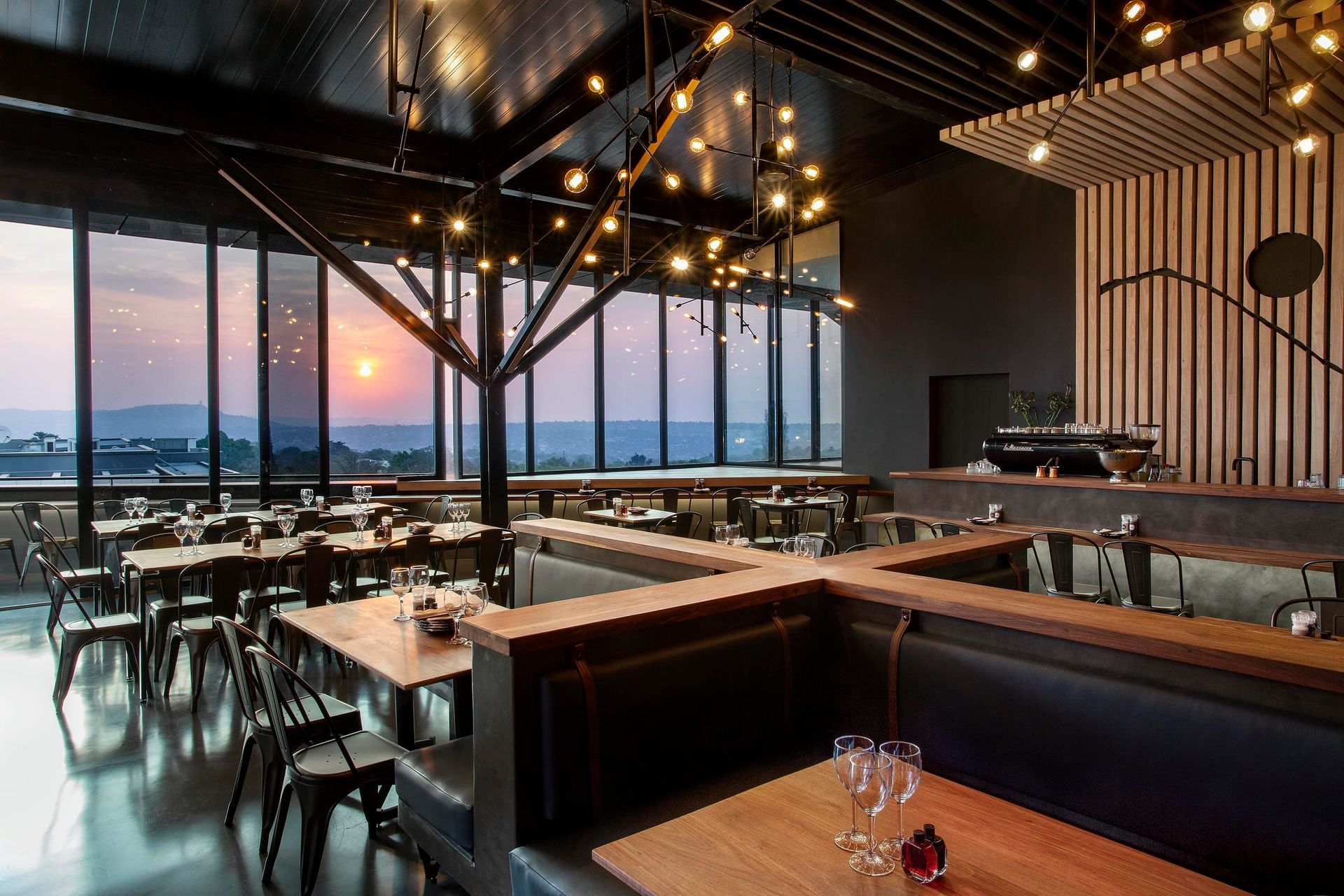 A restaurant with a lot of tables and chairs and a sunset in the background
