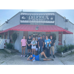 A group of people standing in front of a restaurant called delicious memories