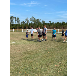 A group of people are standing in a field with a white fence in the background