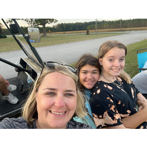 A woman and two girls are sitting in a golf cart.