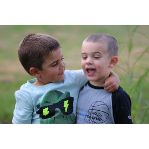 Two young boys are hugging each other in a field.