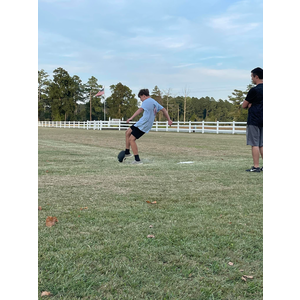 A man is kicking a soccer ball in a field while another man watches.