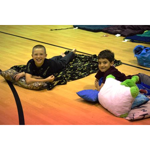 Two boys are laying on the floor with pillows and blankets