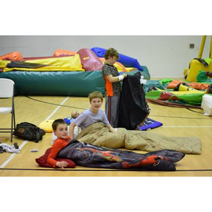 A group of children are laying in sleeping bags on a gym floor