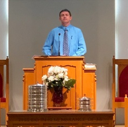 A man stands at a podium in front of a screen that says i will sing the world 's story of the christ