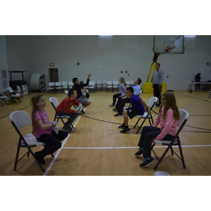 A group of children are sitting in chairs on a basketball court