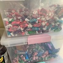 Clear plastic container filled with colorful wrapped candies. A second container holds more candies.