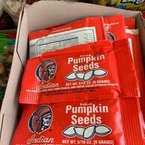 Close-up of several packages of Indian brand salted pumpkin seeds in a cardboard box. Red packaging with the brand logo is visible.