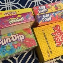 Boxes of candy including Sixlets, Top Pops, Fun Dip, and Swedish Fish on a patterned surface.