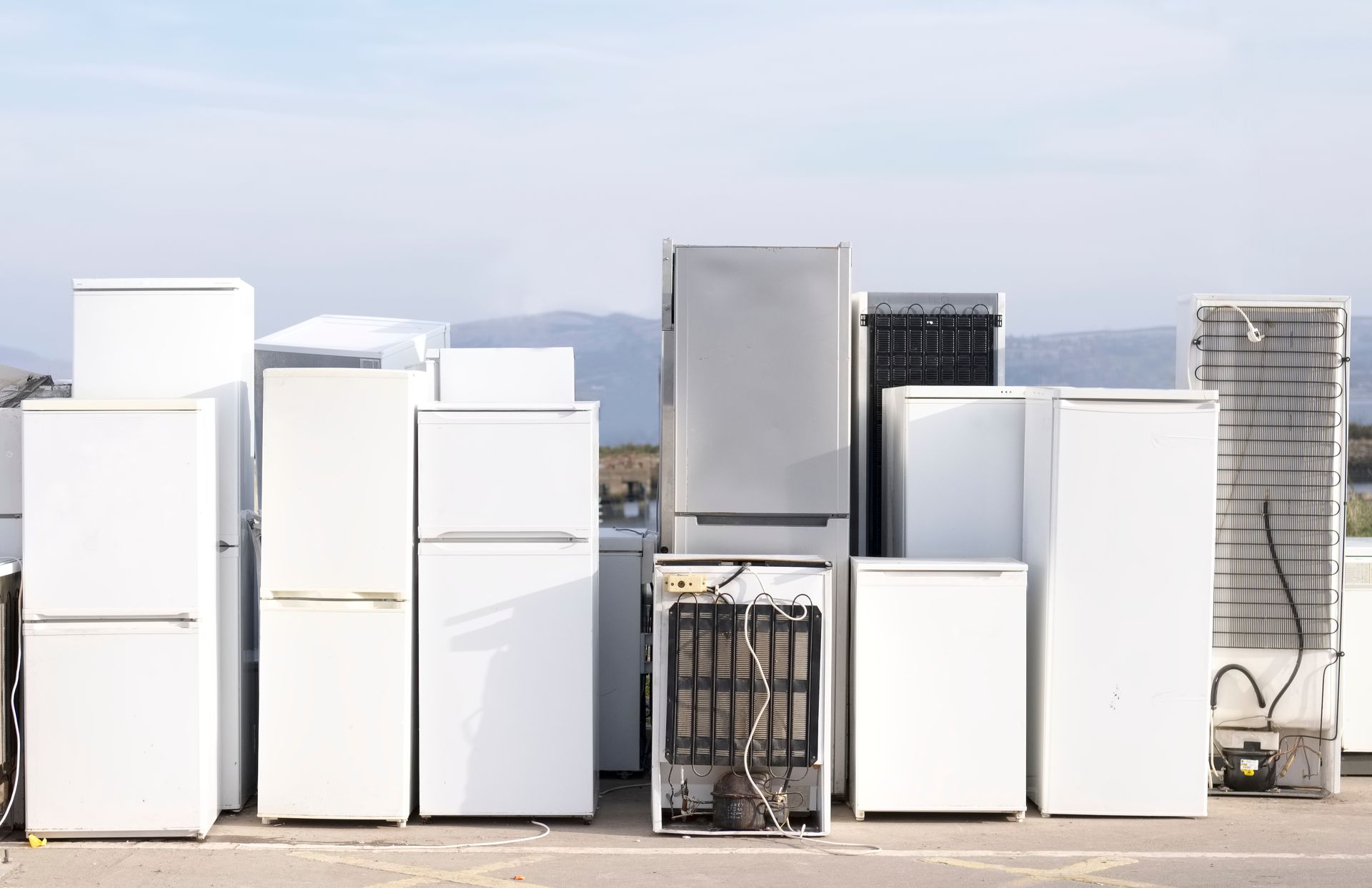 A collection of discarded refrigerators and freezers, outdoors against a cloudy sky. A collection of discarded refrigerators and freezers, outdoors against a cloudy sky.
