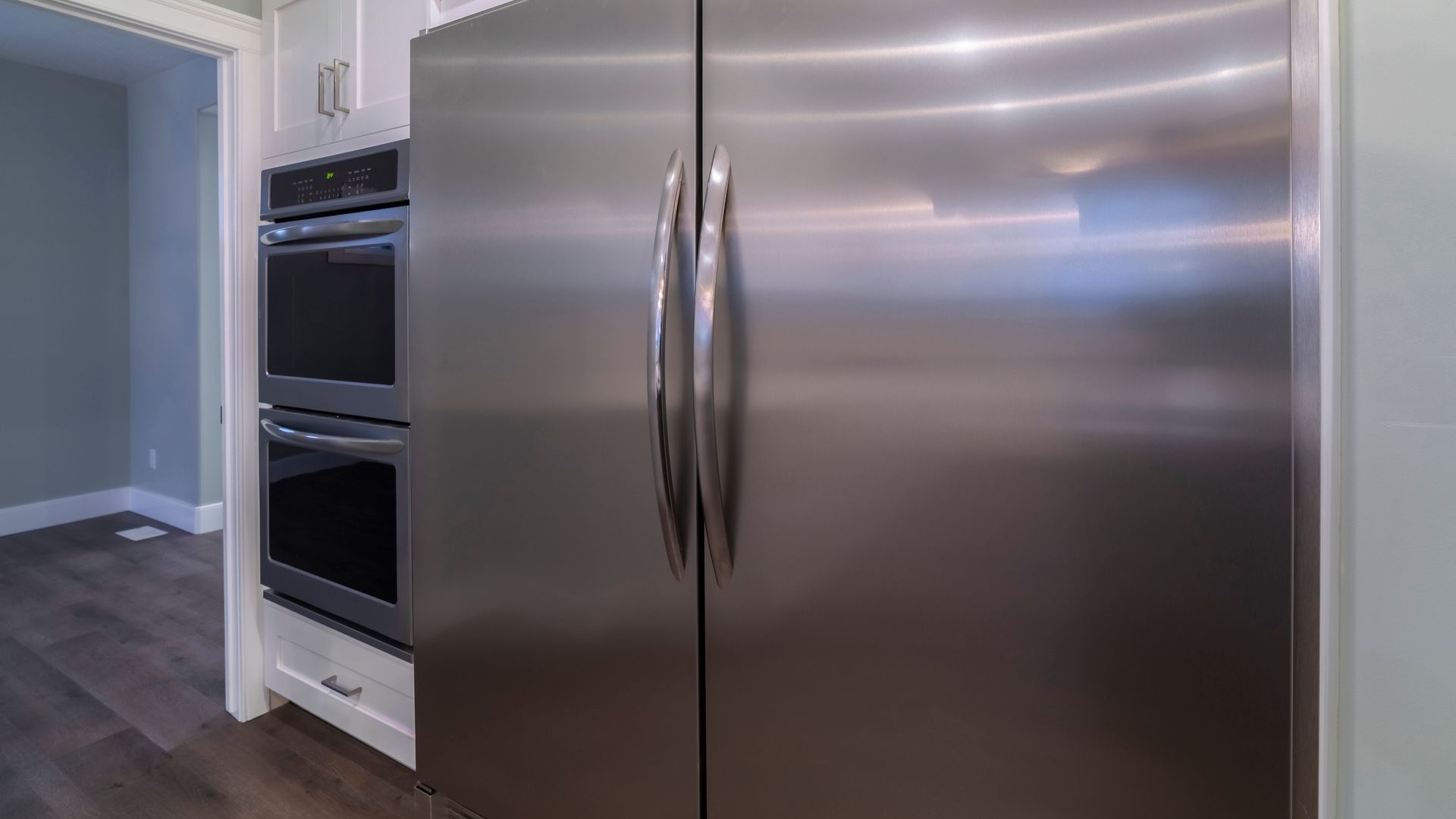 Stainless steel, side-by-side refrigerator in a kitchen with a double oven to the left. Stainless steel, side-by-side refrigerator in a kitchen with a double oven to the left.