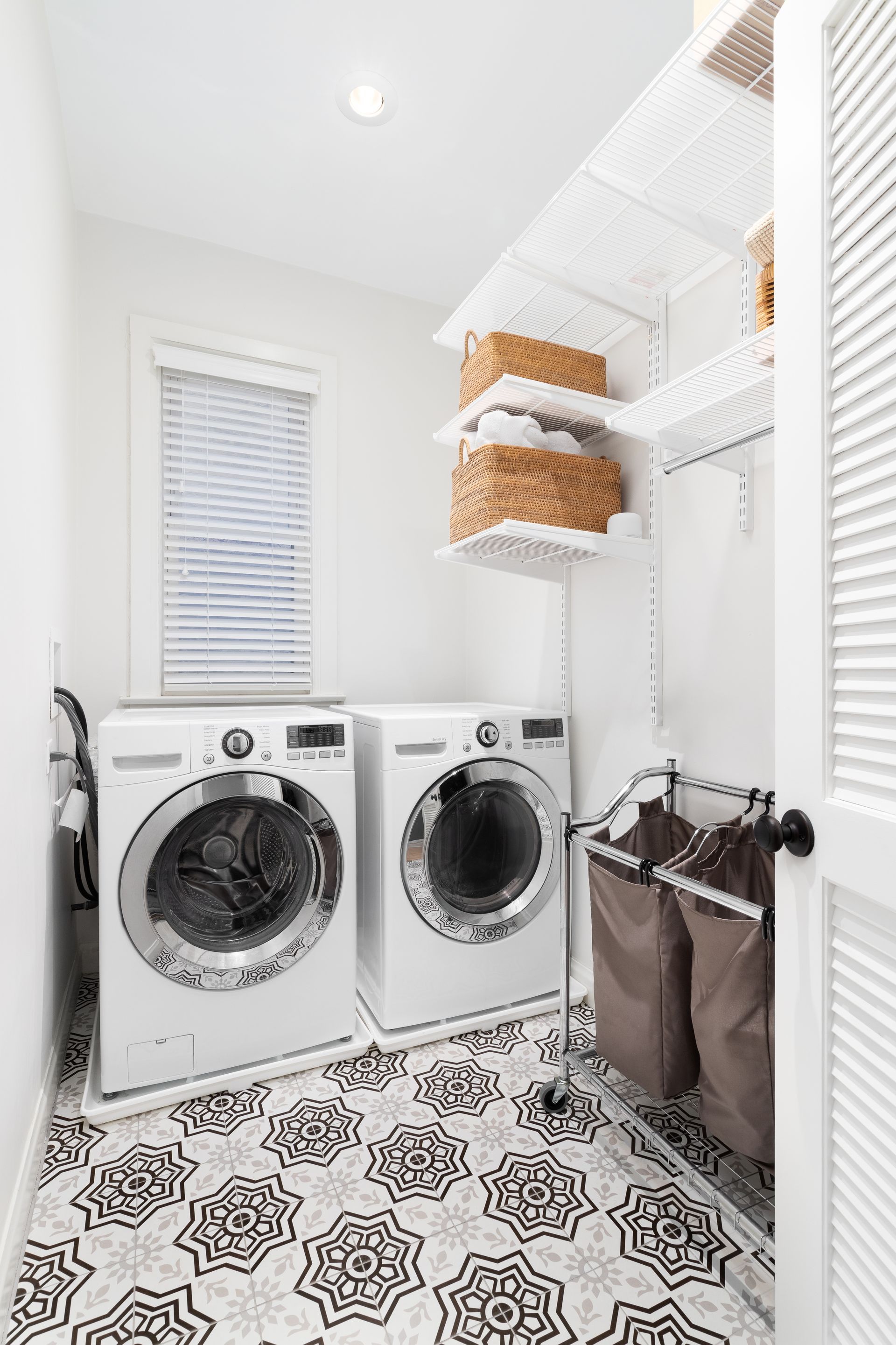 A laundry room with white washer and dryer, a patterned tile floor, and organized shelving on the wall. 